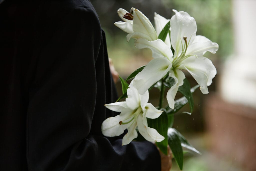 Rain Wet White Lilies in Hands of Person in Black Suit sorg arv begravelse