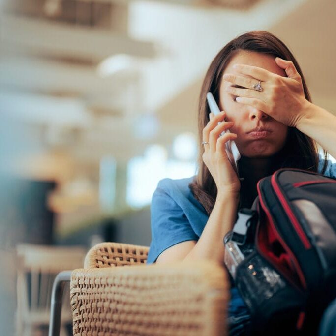 Unhappy Woman Talking on the Phone Waiting in an Airport Stressed traveler speaking on her cellphone feeling overwhelmed