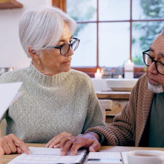 Couple, documents and reading for insurance in retirement, planning and bills or paperwork. Senior people, marriage and communication or discussion for future, saving and finance in kitchen at home