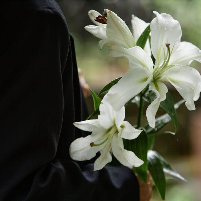 Rain Wet White Lilies in Hands of Person in Black Suit sorg arv begravelse